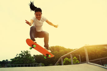 A smiling young girl does an ollie move at a skateboard park.