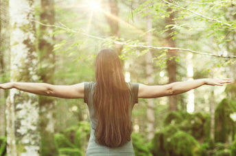 A woman in a forest spreads her arms out wide, showing balance and harmony.
