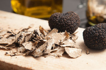 Black truffles and shaved truffles on a wooden cutting board.