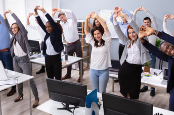 A group of office workers stand and stretch at their desks.