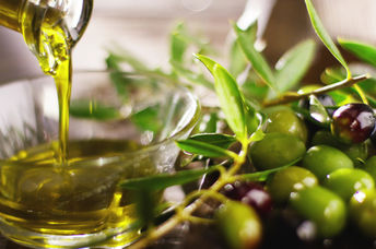Pouring cold pressed olive oil into a bowl beside a branch of olives.