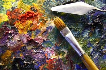 An artist’s palette with colorful paints, palette-knife, and brushes.