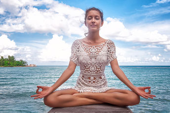 A woman meditates on a dock by a lake.