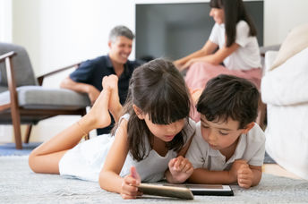 Cute kids lying on floor in living room and using digital gadgets
