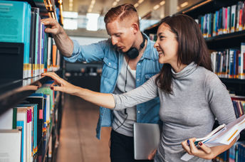 Two young students getting books from a public library shelf.