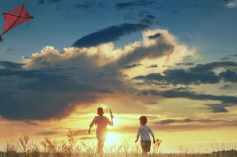 Children launch a kite in a field at sunset