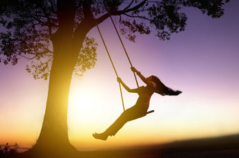 Silhouette of joyful woman on a swing with sunset background