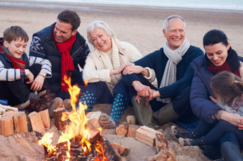 Grandparents, parents, and children connect by enjoying time together around a beach bonfire.