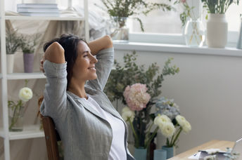 A woman feels calm and relaxed in her mindful workspace surrounded by flowers and soft colors.
