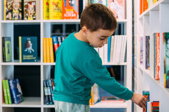 An eight-year-old boy adding his own book to the library bookshelf.