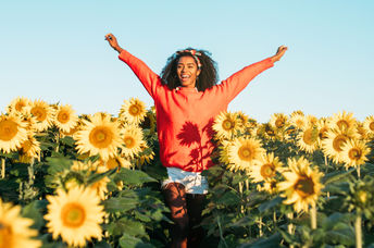 A woman joyfully walks through a field of sunflowers.