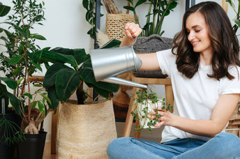 A woman sits on the floor caring for her houseplants.