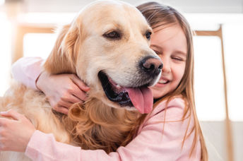 Little girl hugging her golden retriever dog and smiling.