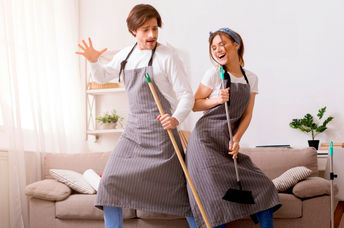 Cheerful couple having fun and dancing while spring cleaning their home.