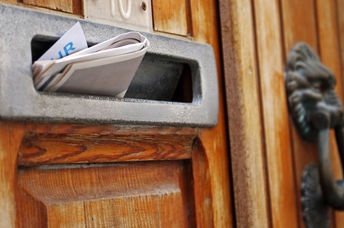 Mailbox filled with rolled spam newspaper in an old wooden door.