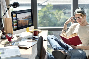 Man engrossed in reading a book at his workstation.