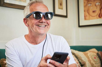A man smiles as he wears augmented reality glasses, seeing subtitles of a conversation.