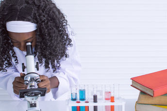Young girl studying science and using microscope in classroom at school
