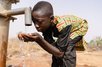 African boy drinking water from a tap.