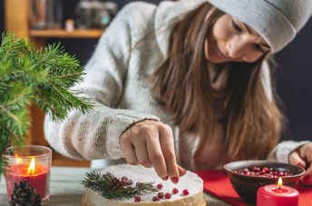 A woman decorating a festive cake with red berries.