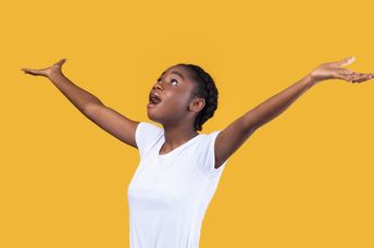 An amazed woman looks up with her hands raised.