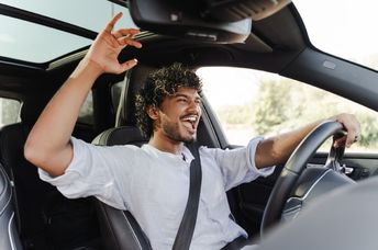 A young man happily drives while singing to music.