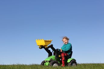 A happy young girl plays on a toy tractor.