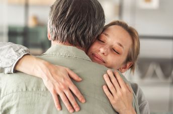 An adult daughter hugs her father.