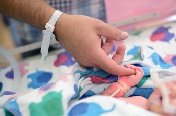 A first-time dad holds the tiny finger of his newborn who needed a little help breathing so was in the NICU.