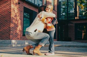 A mother kneels down to hug her daughter.
