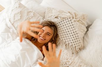 A woman lies in a white cozy bed.