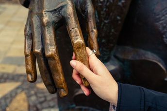 A visually impaired woman feels the hand of a bronze sculpture.