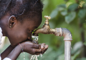 A young African girl drinking clean water from a tap