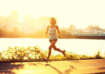 female runner running at sunset in city park.