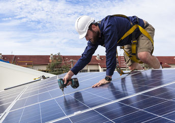 Solar panel technician with drill installing solar panels on roof