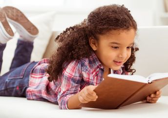 Young girl with curly hair reading a book on the floor