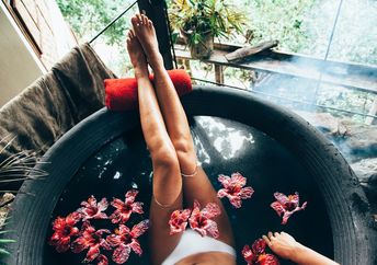 Woman relaxing in round outdoor bath with tropical flowers. Organic skin care in kawa hot bath in luxury spa resort.