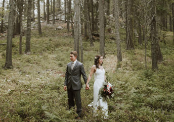A couple in wedding dress and suit stand in the forest.