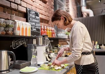 happy woman or barmaid cooking at vegan cafe