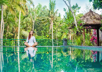 Woman meditation at gorgeous pool side of luxury tropical villa