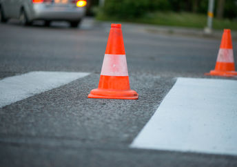 Macro shot of road traffic cones with orange and white stripes standing on street on gray asphalt during road construction works. Just painted white street lines on pedestrian crossing