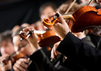 Symphony orchestra first violin section performing on dark background