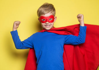 A young boy wearing a superhero mask and cape flexes his muscles and feels strong.