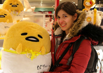 Young woman holds a large Gudetama plush toy.