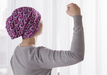A cancer patient raises her arm victoriously, showing positivity.