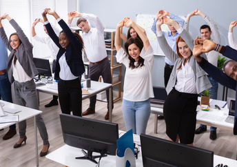 A group of office workers stand and stretch at their desks.