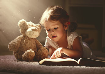 Girl reading to teddy bear.