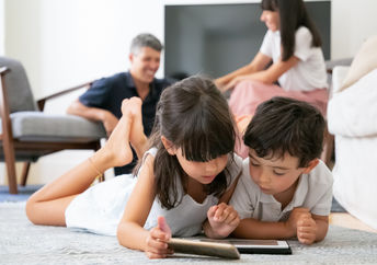 Cute kids lying on floor in living room and using digital gadgets