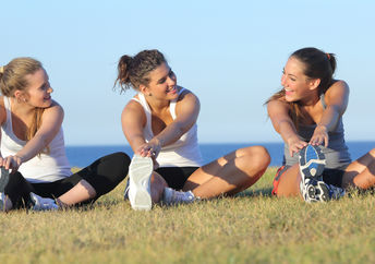 Group of three health-conscious women stretching after sport on the grass