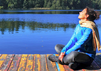 A woman sitting on a dock by a lake is doing a breathing exercise to help tone her vagus nerve.